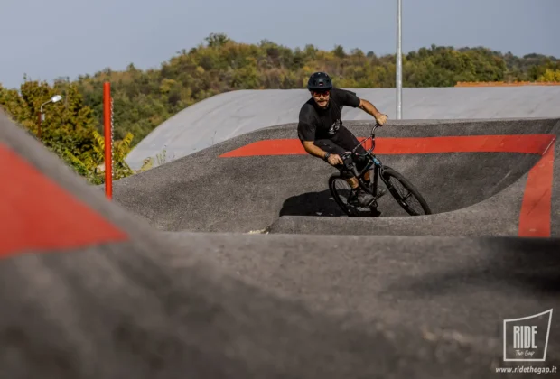 Biker in curva su un pump track in cemento con linee rosse, colline boscose sullo sfondo — Pump Track Bocca di Valle