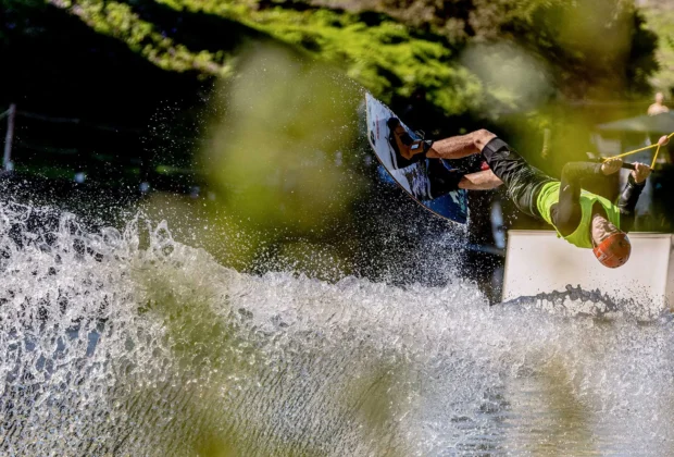 Wakeboarder capovolto in un salto acrobatico su un modulo del cable park, con un grande spruzzo d'acqua durante i Campionati Italiani Assoluti di Wakeboard al Wake N Lake