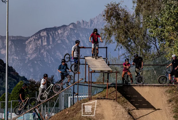 Gruppo di rider BMX in fila sulla rampa di partenza in legno del Bike Park Valgredirt, con le montagne della Valgreghentino sullo sfondo