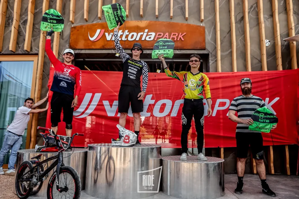 Podio della qualifica UCI Pump Track al Vittoria Park, con i tre atleti che festeggiano davanti al banner dell'evento